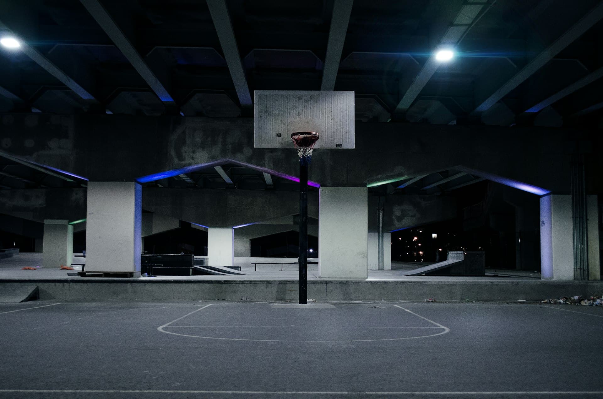 Empty outdoor 3x3 basketball court lit up at night under a bridge